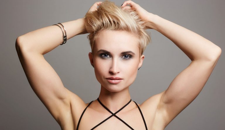 A blond woman with short hair posing on a gray background.