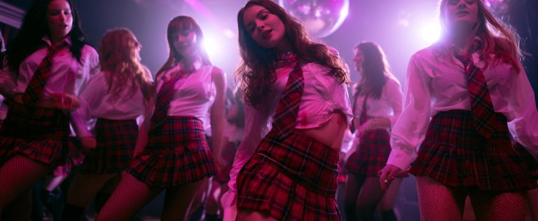 A group of young women in plaid skirts, Wolford tights, and white shirts dance together under pink and purple lights at Pink Punters, a popular UK crossdresser nightclub.