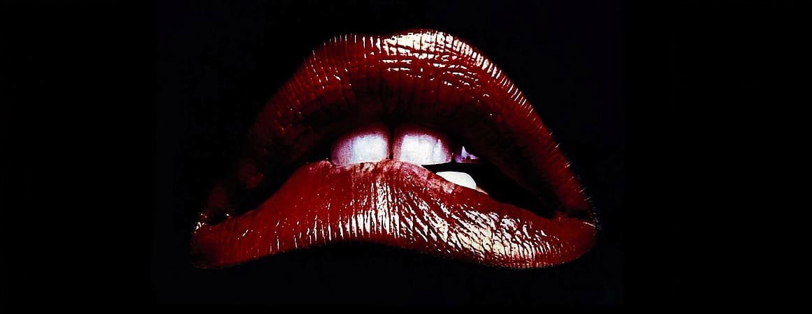 Close-up of glossy red lips with slightly parted white teeth against a black background.